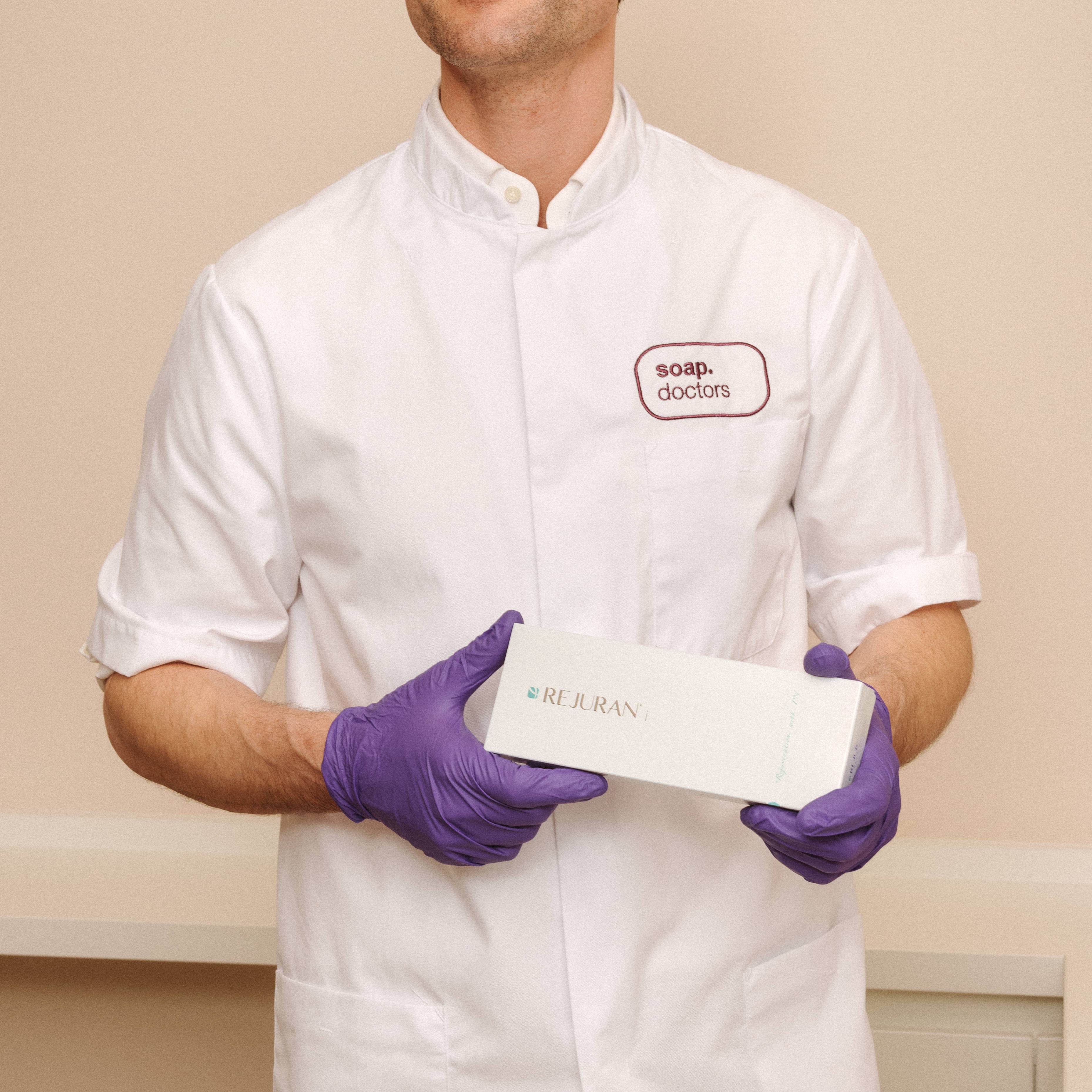 A person in a white coat and purple gloves holds a box labeled "Rejuran" with "soap. doctors" embroidered on the coat.