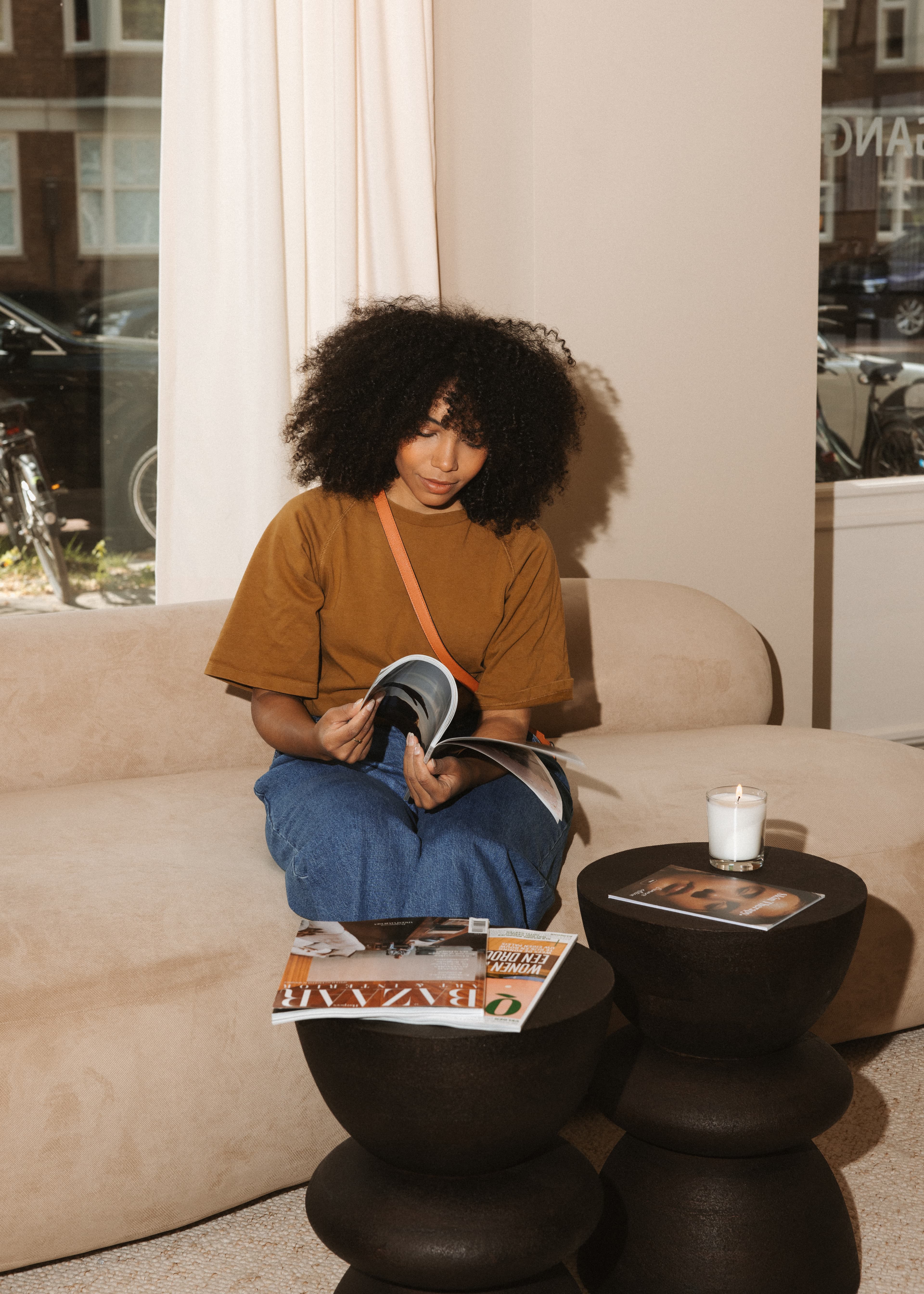 Vrouw met krullen leest een magazine op een lichte bank