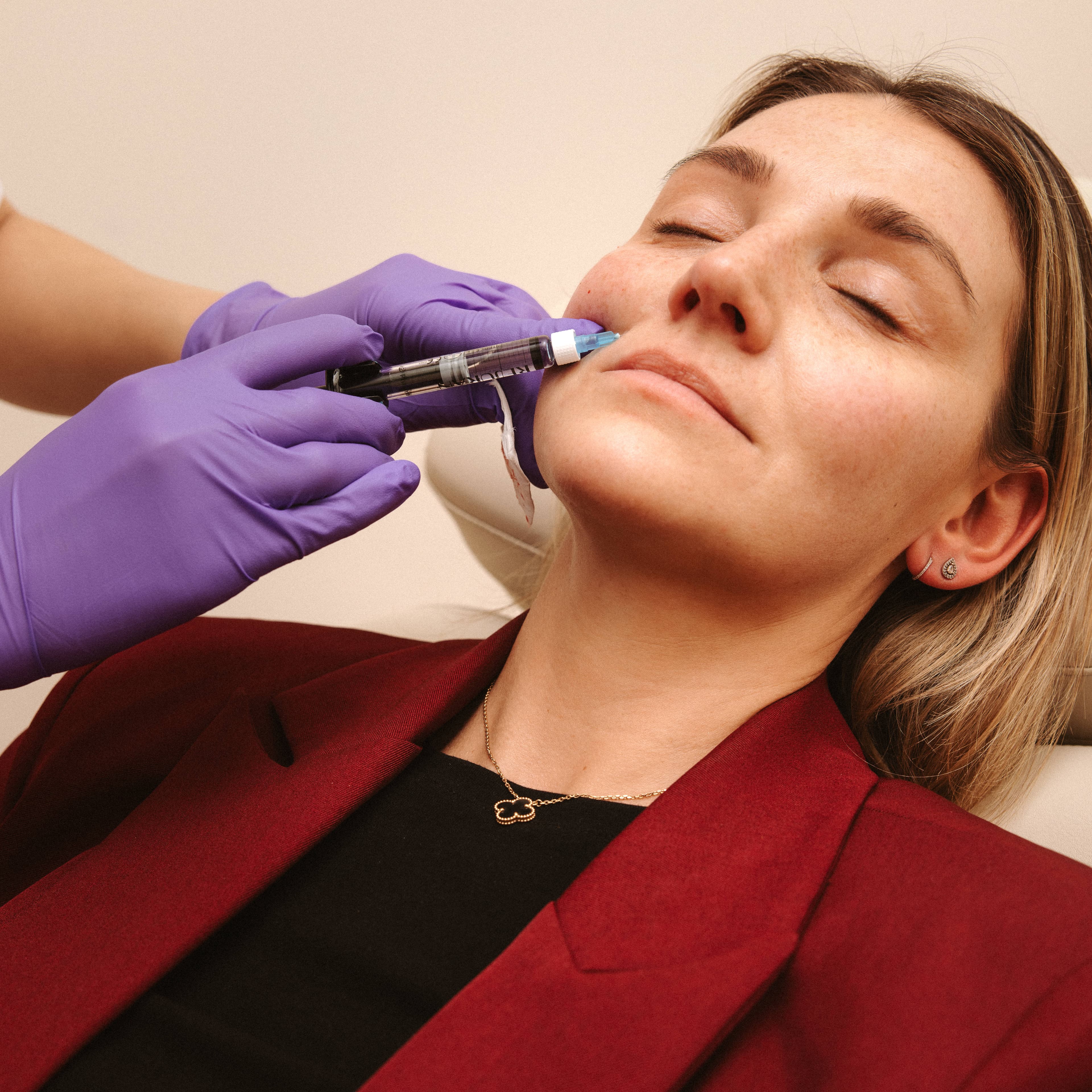 A woman with closed eyes receiving a facial injection from a gloved professional.